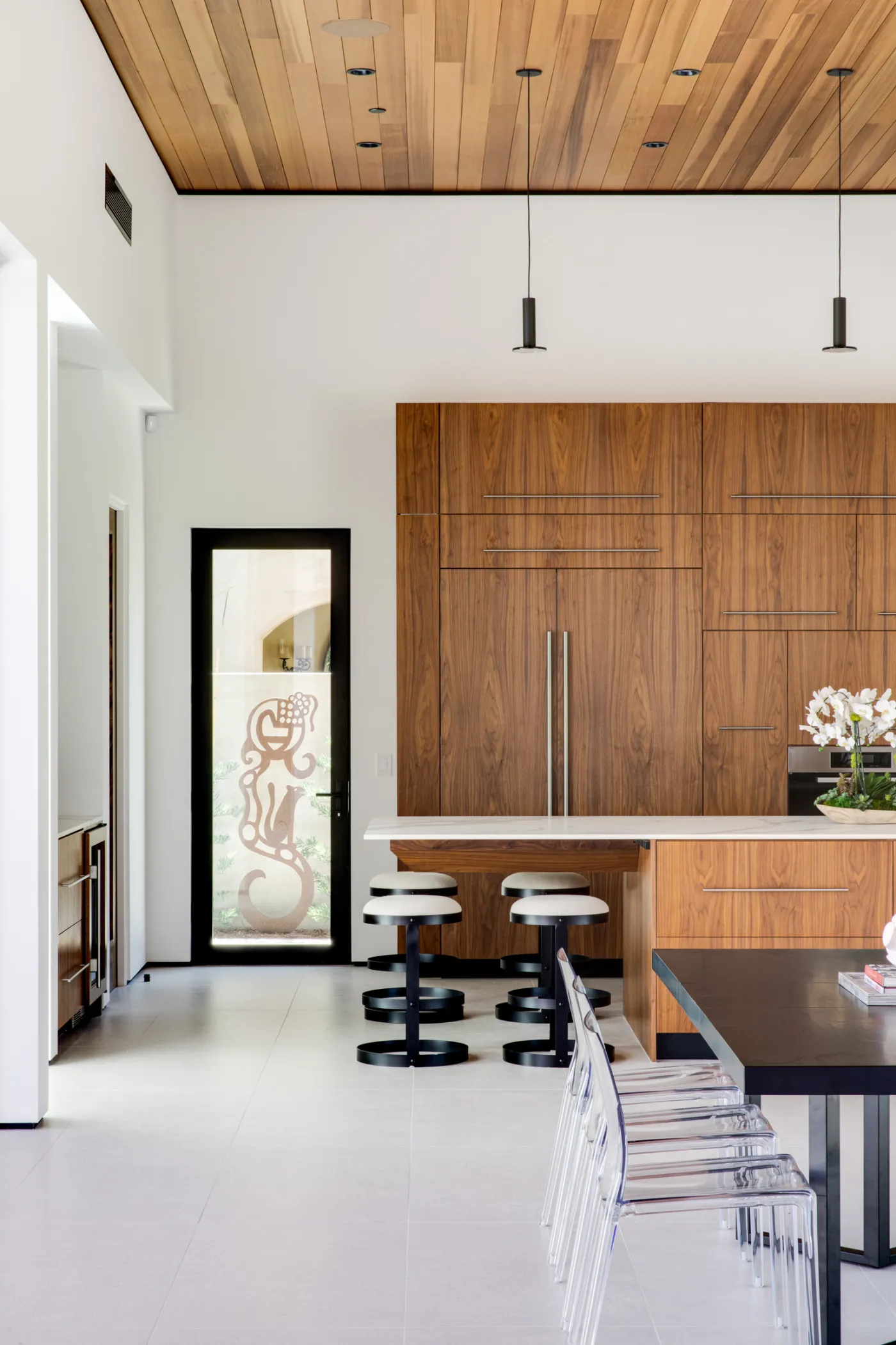 Kitchen with walnut cabinetry, a stone-topped island and black bar stools under a wood ceiling