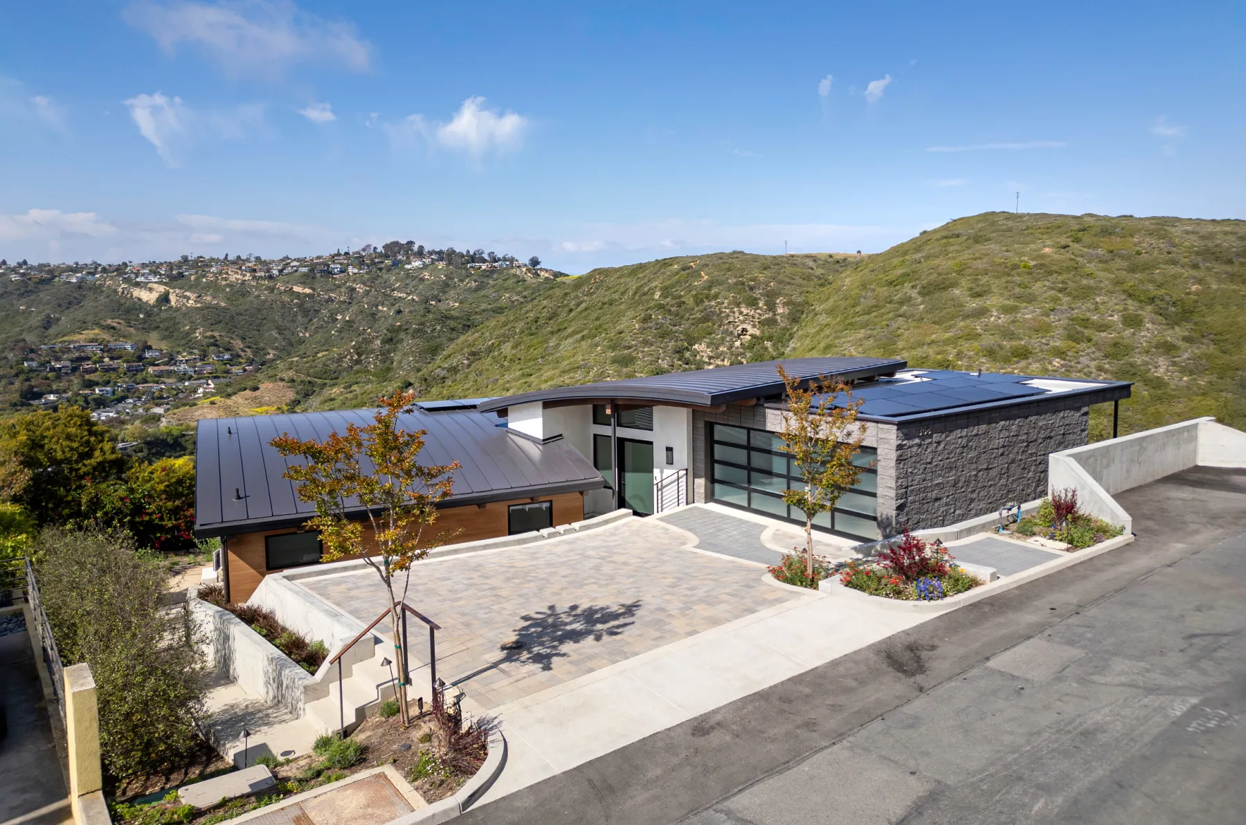Modern hillside home with a dark metal roof and paved motor court